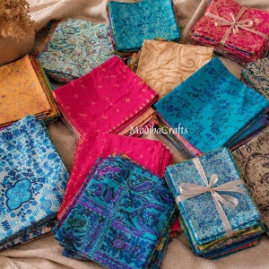 May include: A collection of square fabric pieces in various colors including blue, pink, yellow, and beige, featuring diverse floral and paisley patterns. Some stacks are tied with white ribbon, and the text MadihaCrafts is visible in the center.