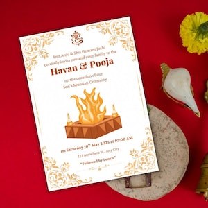 May include: An invitation card for a Havan & Pooja ceremony, with gold floral designs and text. The card includes event details, such as the date, time, and location. The background is red, with decorative items.