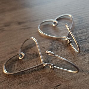 Puede incluir: Un par de pendientes de alambre en forma de coraz&oacute;n de plata. Los pendientes est&aacute;n hechos de alambre fino y tienen un dise&ntilde;o simple y minimalista.