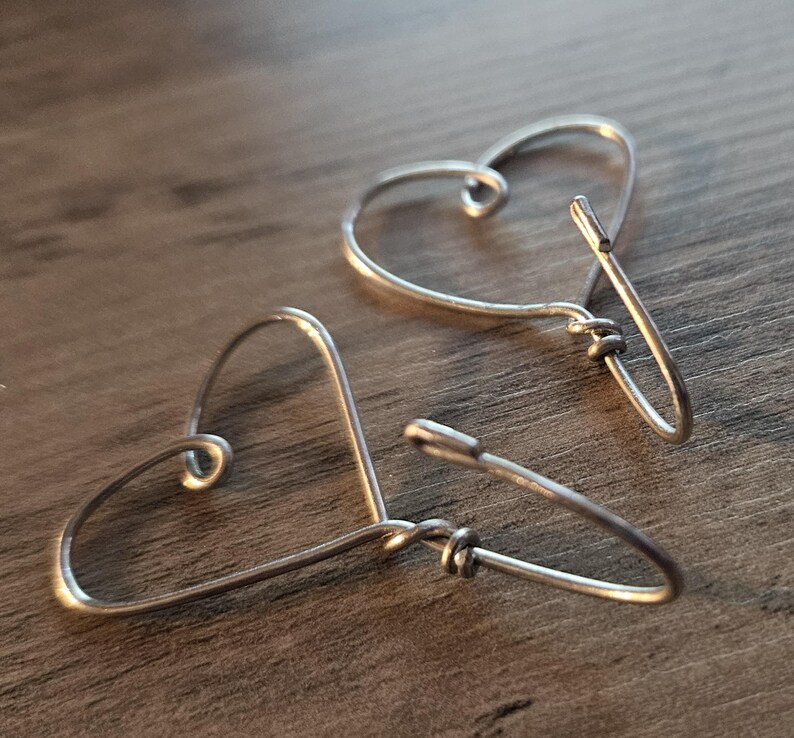 Puede incluir: Un par de pendientes de alambre en forma de coraz&oacute;n de plata. Los pendientes est&aacute;n hechos de alambre fino y tienen un dise&ntilde;o simple y minimalista.