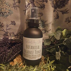 May include: A dark brown glass bottle with a black spray top. The bottle is labeled "Naturals by Alisa Botanical Balance Toner" and lists the ingredients as "Rose Water, Witch Hazel,  Calcuom,  Essential Oil Blend (Chamomile & Lavender)".