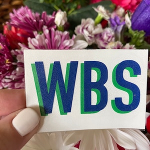 May include: A white sticker with the letters "WBS" in blue and green outlined letters.