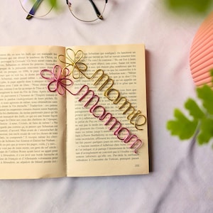 Peut inclure: Un marque-page en fil de fer rose et or avec le mot "Mommie" écrit en cursive. Le marque-page est posé sur un livre avec du texte en français.