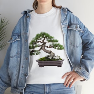 Può includere: Una maglietta bianca con un albero bonsai verde stampato sul davanti. Il bonsai è in un vaso marrone e ha una base di muschio verde.