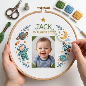 May include: Embroidered hoop art featuring a baby's photo, the name "JACK", and the date "25 AUGUST 2025". The design includes an astronaut, planets, a rocket, and a crescent moon, all in colorful thread. A wooden embroidery hoop holds the artwork.