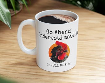 May include: White ceramic coffee mug with a black rooster illustration and the text "Go Ahead Underestimate Me That'll Be Fun".