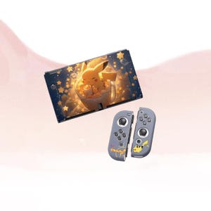 May include: A Nintendo Switch console with a Pikachu-themed design. The screen features a cartoon Pikachu in a cup, surrounded by stars. The Joy-Con controllers are gray with Pikachu graphics and the word "Pikachu".