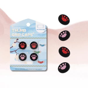 May include: Thumb grip caps for N-Switch 2, featuring a paw print design. The caps are black with red and pink paw prints. The packaging is light blue with the text "THUMB GRIP CAPS" and "For N-Switch 2". The caps are soft, comfortable, dirt-resistant, and wear-resistant.