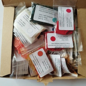 May include: A box filled with small bags of candle wax dye and fragrance. The bags are labeled with the brand name "Candles Fantasy" and the color or scent of the product. The colors include red, orange, white, turquoise, and black.
