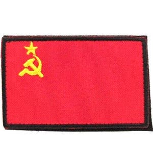 May include: A rectangular red patch with a black border. The patch features a yellow hammer and sickle symbol with a star in the upper left corner. The patch is likely an emblem or insignia.