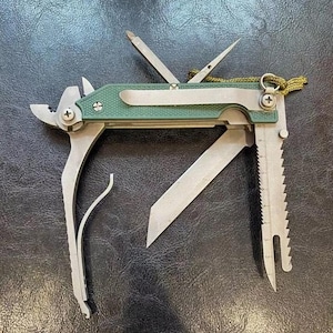 May include: A multi-tool with a green handle and various stainless steel implements, including a saw, knife, and pliers. The tool also features a ruler with inch measurements and a lanyard attachment. The tool is open and displayed on a dark surface.
