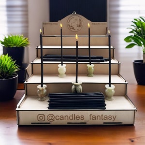 Puede incluir: Un expositor de madera de cinco niveles sostiene velas negras en soportes de mármol verde. El expositor tiene un letrero con el texto "@candles_fantasy" en el nivel inferior.