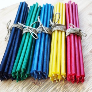 Puede incluir: Un paquete de seis colores de velas de cera de abeja, atadas con un cordel. Los colores son negro, verde, azul, amarillo y rojo.