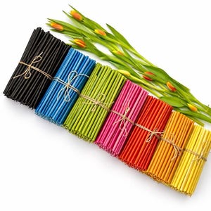 Puede incluir: Paquetes de palitos de madera finos y coloridos atados con hilo. Los colores incluyen negro, azul, verde, rosa, rojo y amarillo. Tulipanes frescos con flores naranjas en el fondo. Palitos decorativos para manualidades o decoración.