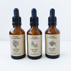 Puede incluir: Tres botellas de vidrio marrón con goteros, cada una contiene un extracto de pino diferente: corteza de pino, aguja de pino y piñas. Cada botella tiene una etiqueta con el texto "The Power of Slovenian Nature" y el nombre del extracto, junto con el volumen (50 ml) y "Handmade in Slovenia".