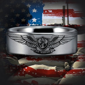 May include: A silver ring with a black and white engraved design of wings and a shield with an anchor and the text "AIR WARFARE".