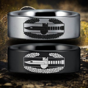 May include: Two tungsten carbide rings with a black and silver finish. The rings feature an engraved design of a military combat infantryman badge.