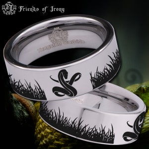 Könnte beinhalten: Zwei silberne Ringe aus Wolframcarbid mit schwarzen Schlangen- und Grasdesigns. Die Ringe sind innen mit "Tungsten Carbide" graviert.