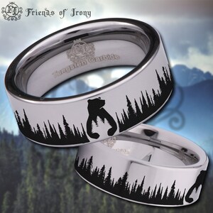 Peut inclure: Une bague en carbure de tungstène argentée avec une silhouette noire d'un ours et de pins. La bague est gravée avec "Tungsten Carbide".