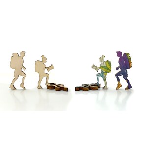 May include: Four wooden figurines of hikers, each with a backpack and walking stick. The hikers are in various poses, some are walking, some are climbing, and some are standing. The figurines are painted in different colors, including brown, green, purple, and blue.