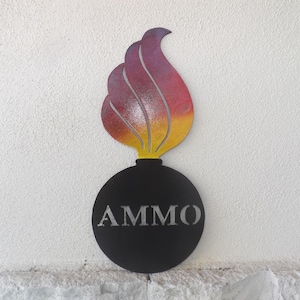 May include: A metal sign in the shape of a bomb with a flame. The flame is painted with a gradient of yellow, orange, and purple. The black bomb has the word "AMMO" in silver letters.