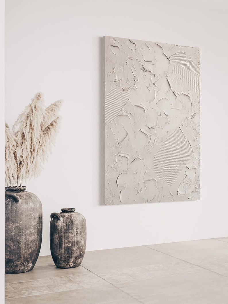 Puede incluir: Dos jarrones de cer&aacute;mica marr&oacute;n con una superficie texturizada, uno m&aacute;s alto que el otro, sobre un suelo de baldosas beige claro. Una gran pintura abstracta con una superficie texturizada en tonos beige cuelga de una pared blanca detr&aacute;s de los jarrones.