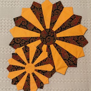 May include: Two handmade, fan-shaped fabric placemats. The placemats feature a vibrant design with alternating sections of yellow dotted fabric and black paisley fabric with red and brown accents. The center of each placemat is a paisley circle.