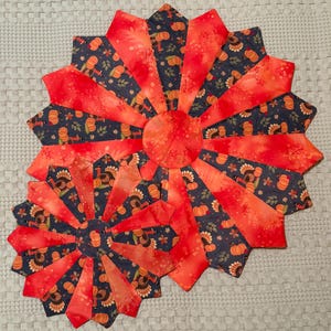 May include: Two decorative, fan-shaped placemats. The placemats feature a vibrant design with alternating red and navy blue segments. The navy blue segments are patterned with pumpkins and turkeys. The center of each placemat is a solid red circle.