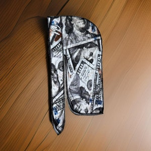 Può includere: Un bandana con motivo bianco e nero con un design di banconote in dollari americani. Il bandana presenta il ritratto di Benjamin Franklin e il testo "100" e "UNITED STATES OF AMERICA".