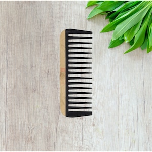 May include: A wooden comb with black plastic teeth. The comb is on a light wood surface.