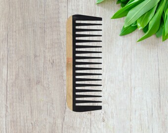 May include: A wooden comb with black plastic teeth. The comb is on a light wood surface.