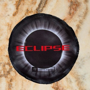 Peut inclure: Un patch circulaire noir et blanc avec une image d'éclipse noire au centre. Le mot "ECLIPSE" est écrit en lettres rouges au-dessus de l'éclipse. Le texte "URBAN EFFECT" est écrit en lettres blanches sous l'éclipse.