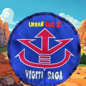 Peut inclure: Un patch circulaire bleu et rouge avec le texte "URBAN BALL Z" et "VEGETA SAGA" en blanc. Le patch présente un symbole rouge et blanc avec trois flèches pointant vers le haut.
