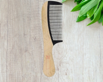 May include: A wooden comb with black teeth. The comb has a rounded handle and is made of natural wood.