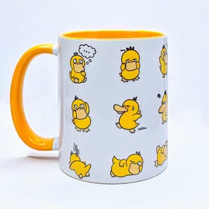 May include: White ceramic mug with a yellow interior and handle. The mug features a repeating pattern of yellow cartoon ducks in various poses. The ducks have black eyes and beaks. The mug is on a white background.