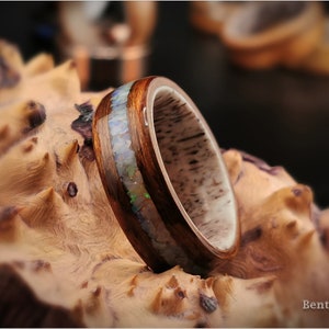 May include: A wooden ring with a band of opal inlay. The ring is set on a piece of wood with a natural grain pattern.