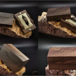 May include: A wooden ring box with a dark brown finish. The box is engraved with the text "BW Dreams" and has a small ring pillow inside. The box is open and the ring pillow is visible.