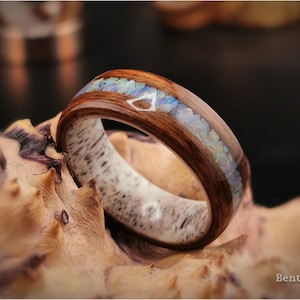 May include: A wooden ring with a band of light brown wood and a strip of dark brown wood inlaid with iridescent opal chips.