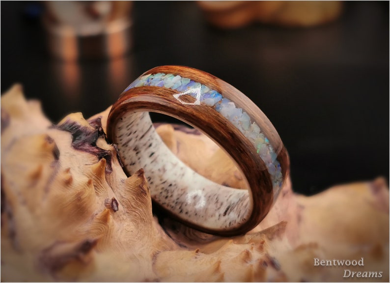 May include: A wooden ring with a band of light brown wood and a strip of dark brown wood inlaid with iridescent opal chips.