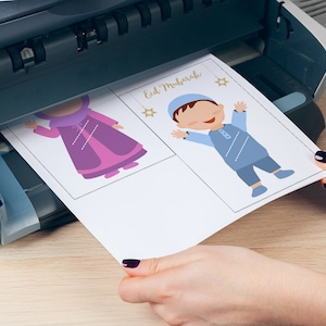 May include: A sheet of paper with two illustrations of children in traditional clothing. The text "Eid Mubarak" is printed at the top of the page. The paper is being fed into a printer.