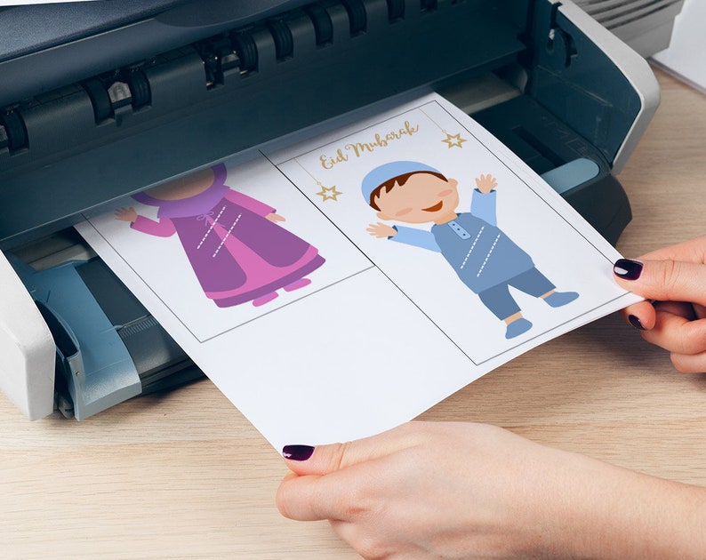 May include: A sheet of paper with two illustrations of children in traditional clothing. The text "Eid Mubarak" is printed at the top of the page. The paper is being fed into a printer.