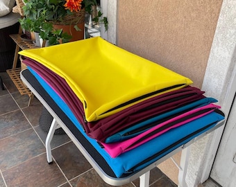 Könnte beinhalten: Ein Stapel bunter Haustierbetten in Gelb, Burgunderrot, Türkis, Pink und Blau. Die Betten sind rechteckig und scheinen aus einem weichen, gepolsterten Material zu bestehen. Sie sind auf einem kleinen Tisch gestapelt.