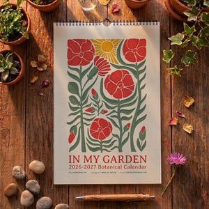 Może przedstawiać: Kalendarz ścienny zatytułowany IN MY GARDEN 2026-2027 Botanical Calendar, przedstawiający graficzną ilustrację czerwonych kwiatów, zielonych łodyg i żółtego słońca na kremowym tle, oprawiony czarną spiralą na górnej krawędzi.