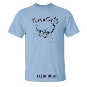 May include: Light blue t-shirt with the text "Turbo Cats" above a cat face graphic. The cat graphic has green eyes and blue accents. The words "Light Blue" are printed at the bottom of the shirt.