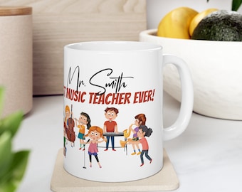 Może przedstawiać: Biały kubek ceramiczny z czarnym uchwytem. Kubek przedstawia kreskówkową ilustrację dzieci grających na instrumentach muzycznych. Tekst "Mr. Smith Best Music Teacher Ever!" jest nadrukowany na kubku czarnym kolorem.