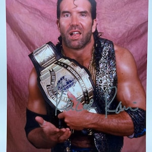 Peut inclure: Photographie en couleur d'un homme tenant une ceinture de championnat de lutte. La ceinture est dorée et noire avec les mots "Intercontinental Heavyweight Champion" et un emblème de globe. L'homme porte un gilet et une chaîne en or.