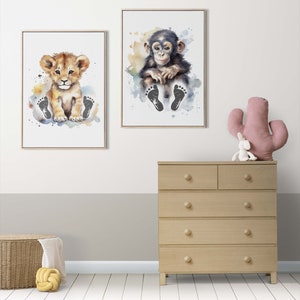 May include: Two watercolor prints featuring animal footprints. The first print shows a lion cub with brown fur and a light brown mane sitting on a light blue background with black footprints. The second print shows a chimpanzee cub with black fur sitting on a light blue background with black footprints.