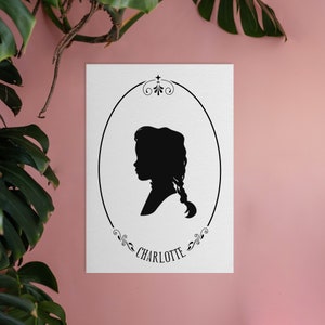 May include: Black and white silhouette of a girl with a braid, inside an oval frame with decorative flourishes. The name "CHARLOTTE" is written below the frame.