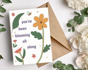 May include: A white card with a floral design and the text "you've been blooming all along". The card features a yellow flower, a red flower, and a bee.