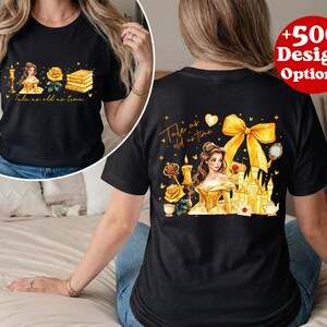 Puede incluir: Camiseta negra con un dise&ntilde;o de "La Bella y la Bestia". El frente muestra una princesa, una rosa, libros y el texto "Tale as old as time". La parte trasera presenta un castillo, un lazo y el mismo texto.